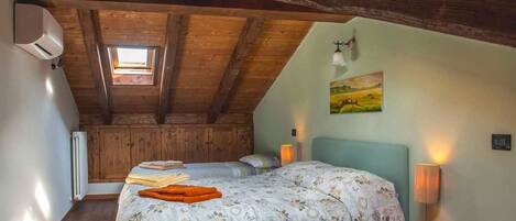 A cozy attic bedroom with a sloped ceiling, a skylight, a bed with floral bedding, a nightstand with a lamp, and a painting on the wall.