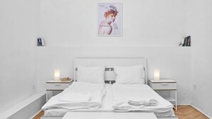 A modern bedroom with a white bed, two bedside tables, a wooden floor, and a black and white striped rug. - Legendary Ernesto II (Budapest)