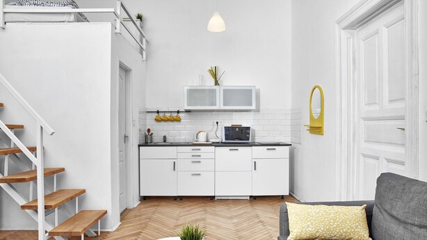 A modern kitchen with white cabinets, a microwave, and a hanging pot rack. - Legendary Ernesto II (Budapest)