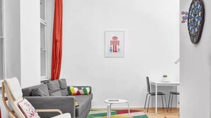 A modern living room with a grey sofa, a wooden chair, a small white table, and a colorful rug. - Legendary Ernesto II (Budapest)