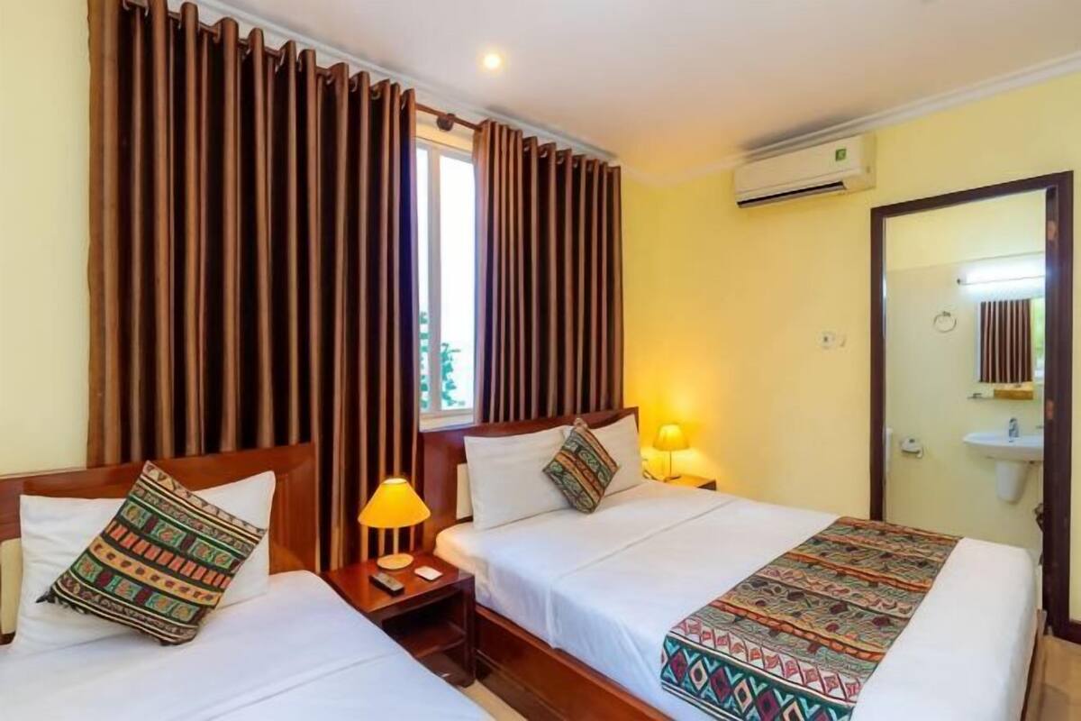 Une chambre d’hôtel avec deux lits, une fenêtre avec des rideaux, un climatiseur, une lampe de chevet et un lavabo.