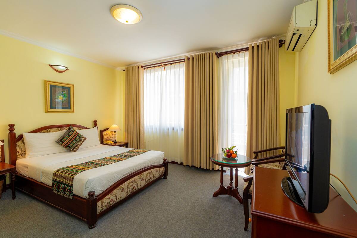 Une chambre d’hôtel avec un lit en bois, une télévision, une petite table avec des fruits et un tableau au mur.