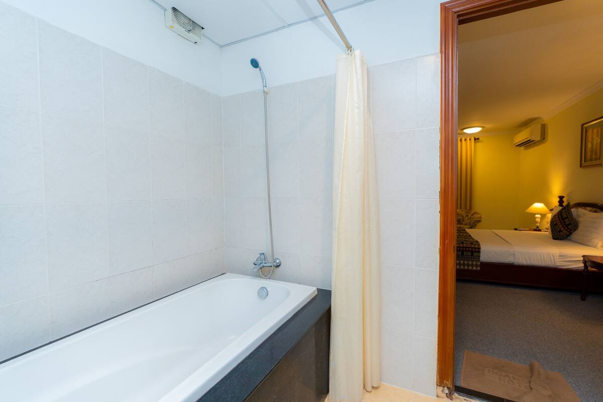 Une salle de bain avec une baignoire, une douche et un lit visible à travers une porte ouverte.