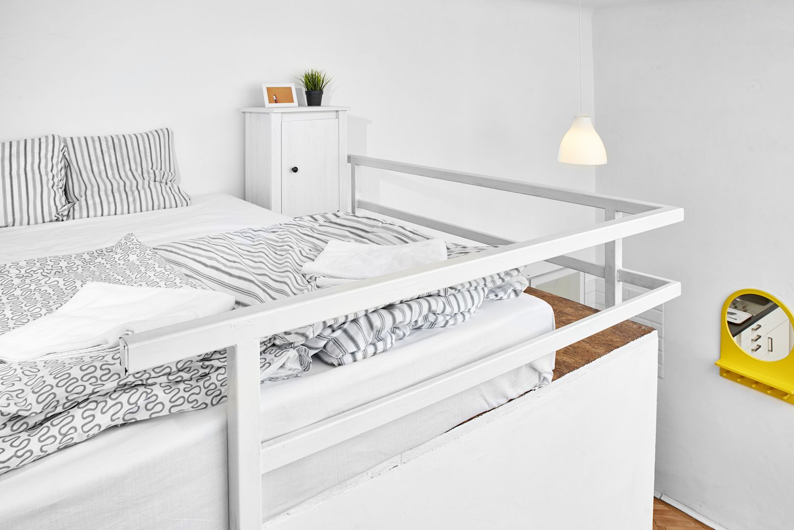 A white bunk bed with striped bedding, a small cabinet with a plant, and a yellow clock on the wall.