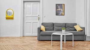 Uma sala de estar moderna com um sofá cinza, uma mesa pequena branca, um vaso de planta e um quadro na parede.