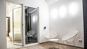 A modern room with a sliding glass door leading to a balcony, two white wireframe chairs, and a small round table. - Hotel New Bari (Bitritto)