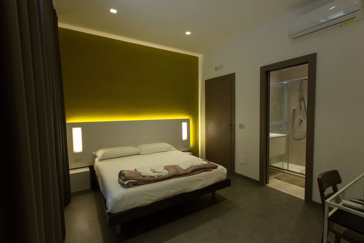 Una habitación de hotel moderna con cama, mesita de noche y zona de ducha.