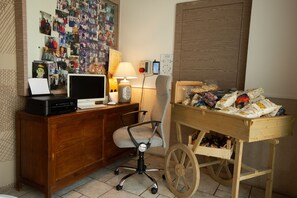 Una habitación con un escritorio de madera, una computadora, una lámpara y un carrito de madera lleno de maletas.