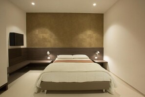Una habitación de hotel moderna con una cama grande, dos mesitas de noche y un televisor de pared.