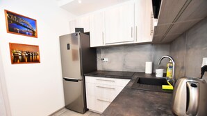 Una cocina moderna con un refrigerador de acero inoxidable, gabinetes blancos, una encimera de granito, un hervidor y dos cuadros en la pared.