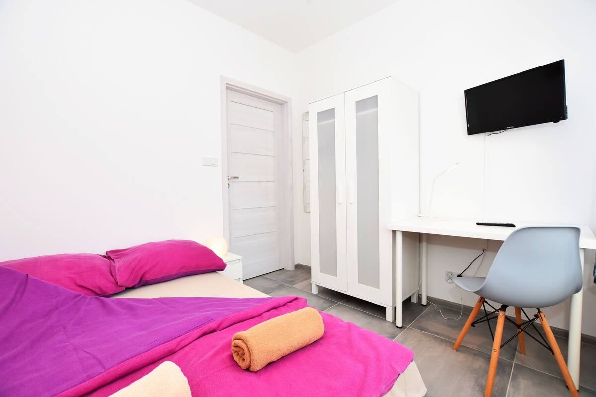 A bedroom with a bed, a desk, a chair, and a television.