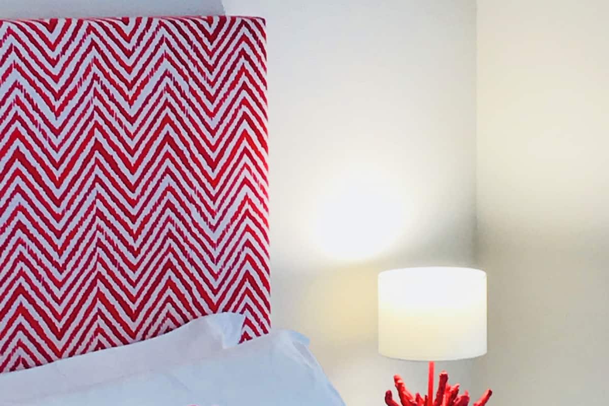 Une chambre d’hôtel avec un lit, des oreillers rouges et blancs, une lampe rouge et un mur à motifs.