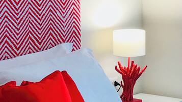 A hotel room with a bed, red and white pillows, a red lamp, and a patterned wall.