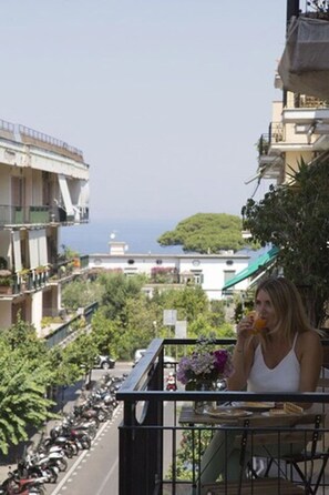 Un balcon avec vue sur la mer, une moto garée et une table avec une boisson.
