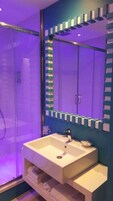 Casa de banho com uma pia branca, um espelho com moldura azul e zona de duche.