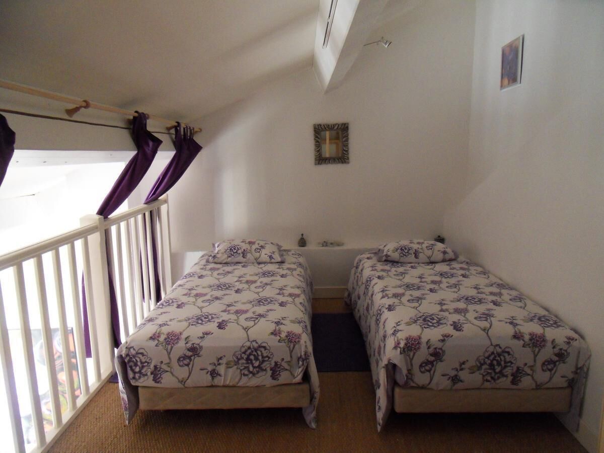 A room with two beds, a small window with curtains, a wall-mounted picture, and a white ceiling.