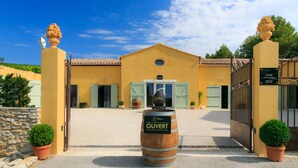 A yellow building with a central entrance, two potted plants on either side, and a barrel with the word "OUVERT" in front. - Chambres d'hôtes Domaine l'Olibaou (Venelles)