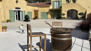 A rustic outdoor seating area with a wooden chair and a barrel, in front of a yellow building with green shutters and a door. - Chambres d'hôtes Domaine l'Olibaou (Venelles)