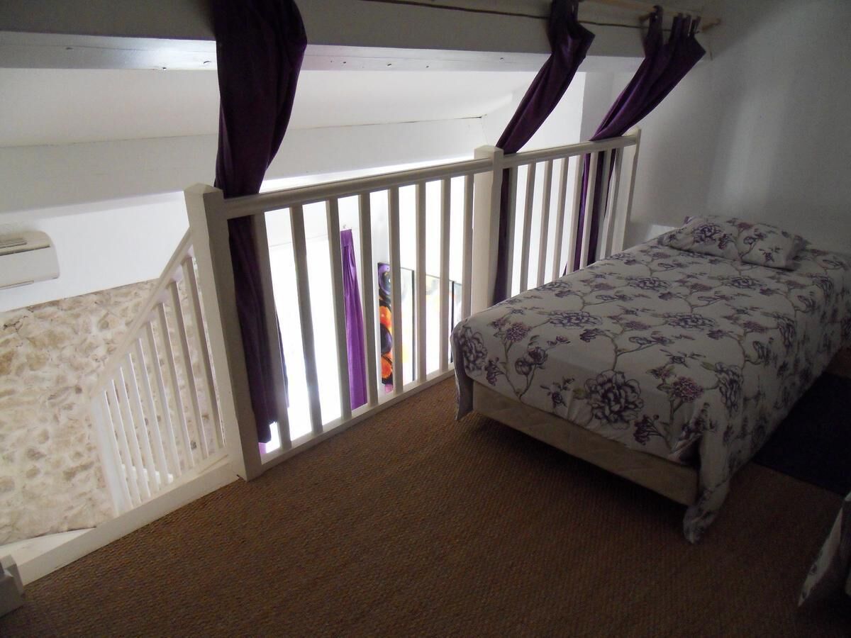 A bedroom with a bed, a window with curtains, a white railing, and a carpeted floor.