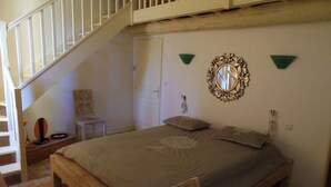 A bedroom with a wooden bed, a white staircase, a mirror, and a small table. - Chambres d'hôtes Domaine l'Olibaou (Venelles)