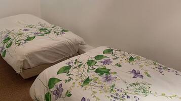 Una habitación con dos camas, cada una con ropa de cama floral. Hay cuadros en la pared y una pequeña obra de arte enmarcada sobre las camas.