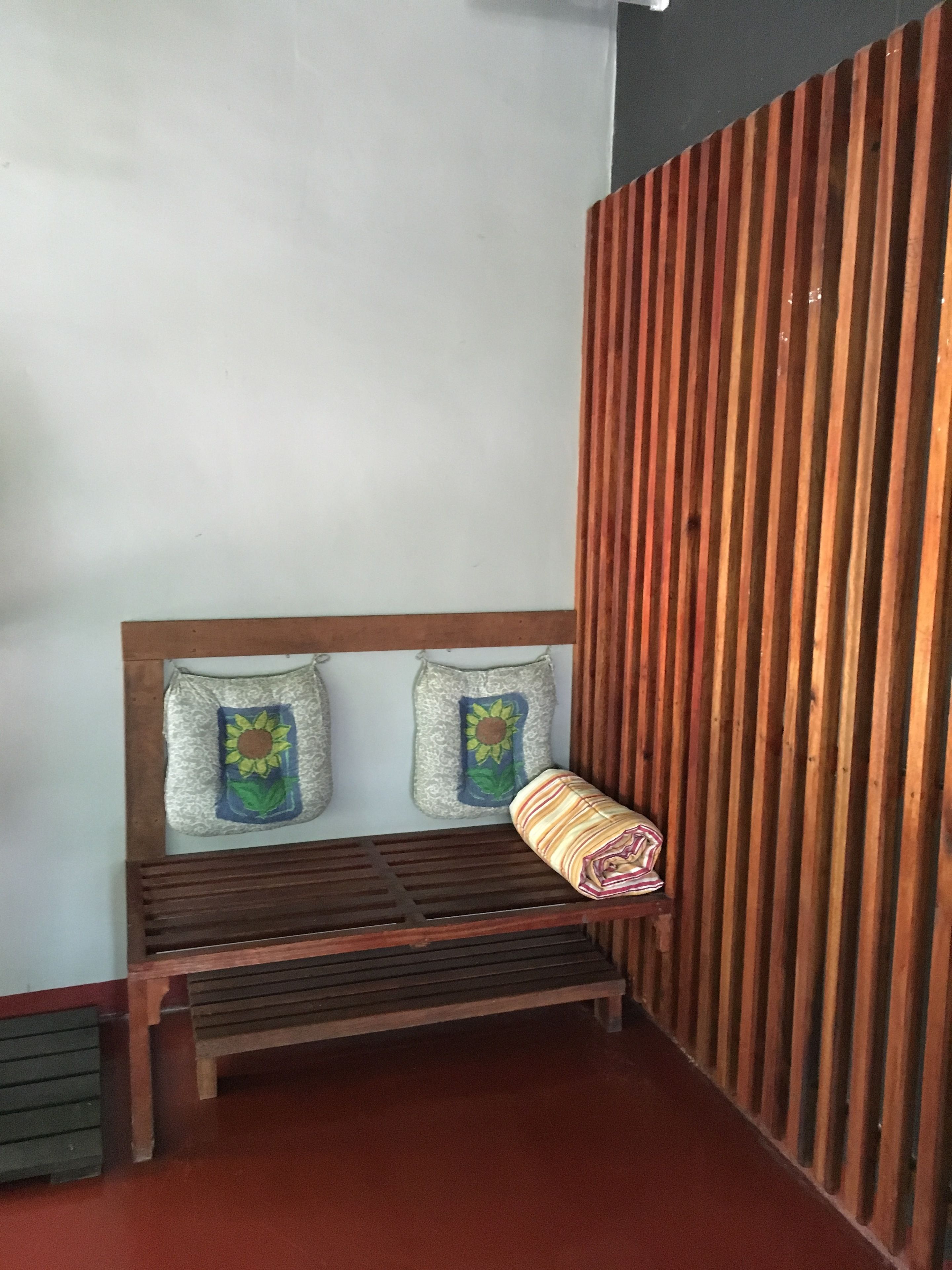 A wooden bench with two pillows featuring sunflowers, against a wall with vertical wooden slats.