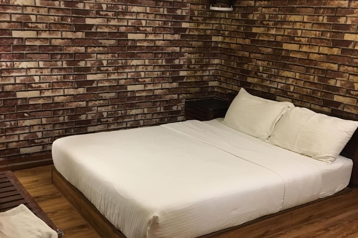 A bedroom with a brick-patterned wall, a wooden floor, a bed with white bedding, and a nightstand with a plant.