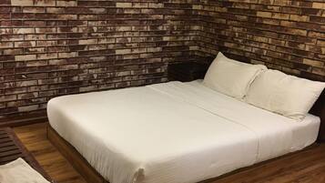 A bedroom with a brick-patterned wall, a wooden floor, a bed with white bedding, and a nightstand with a plant.