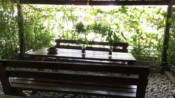 Ein Holztisch mit einer Schale und einer Glasvase, platziert auf einer Bank unter einer Pergola mit Blick auf dichtes Grün.