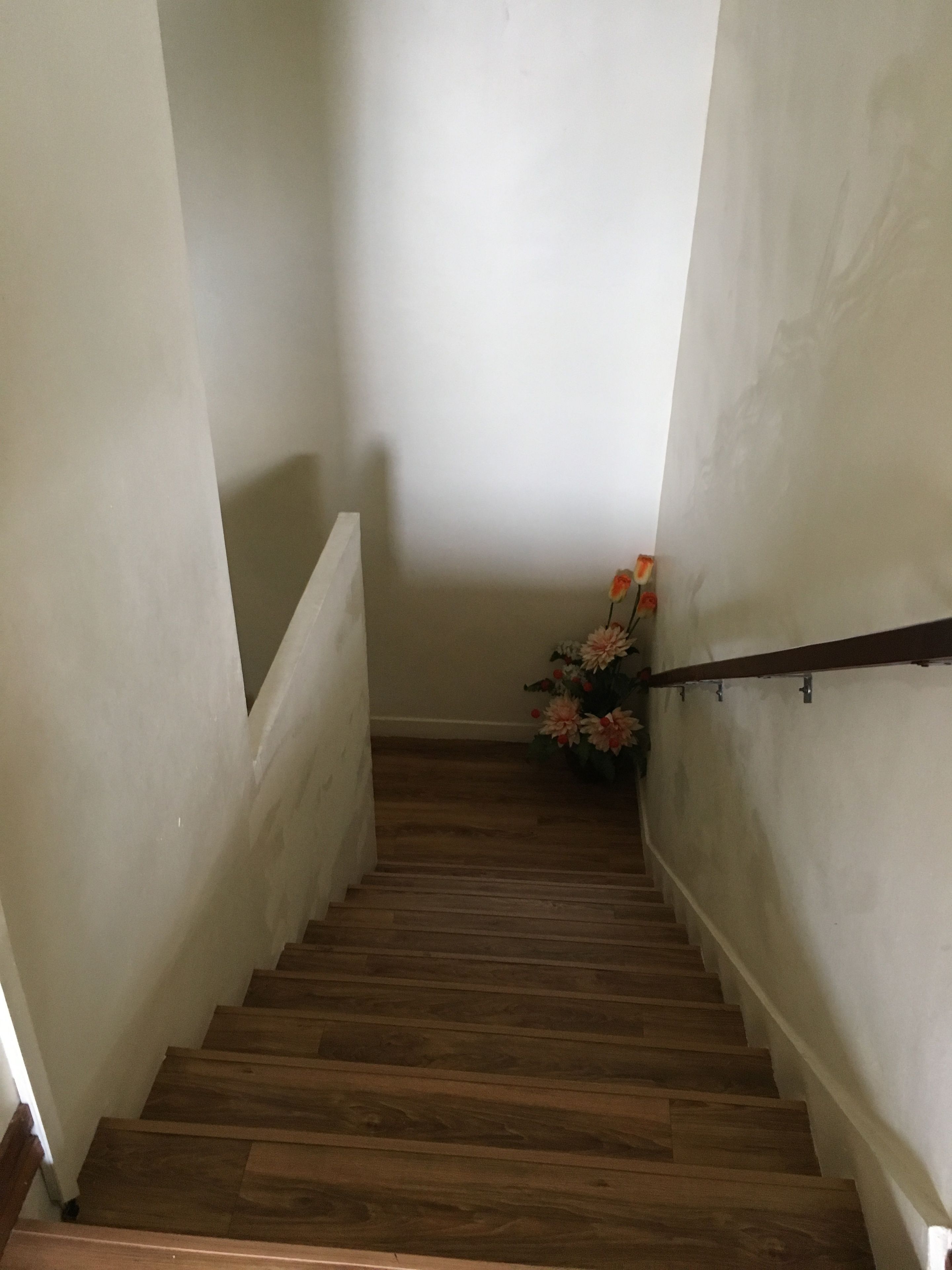 A wooden staircase with white walls and a handrail.