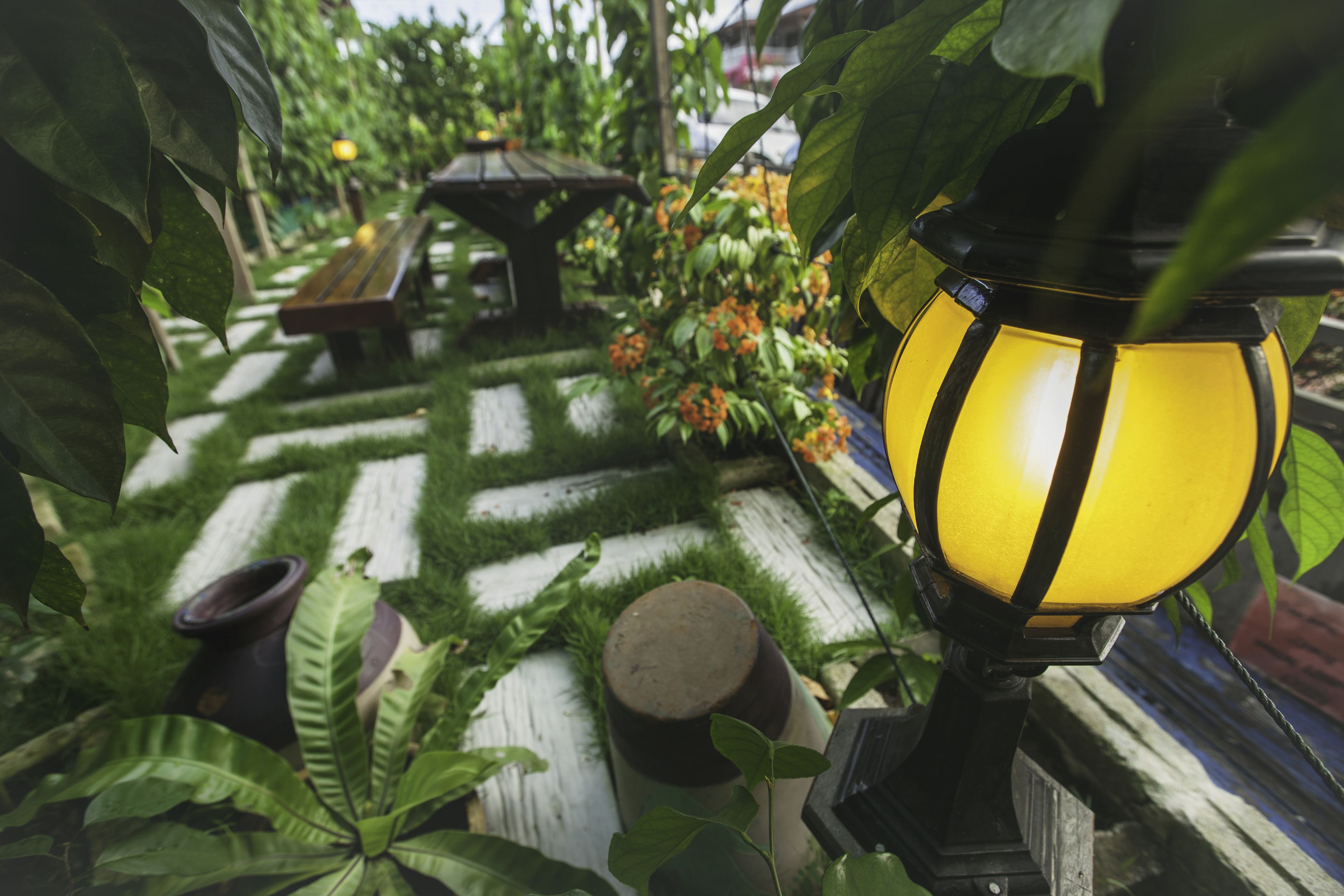 Un sentier de jardin avec un banc, une table et un lampadaire.