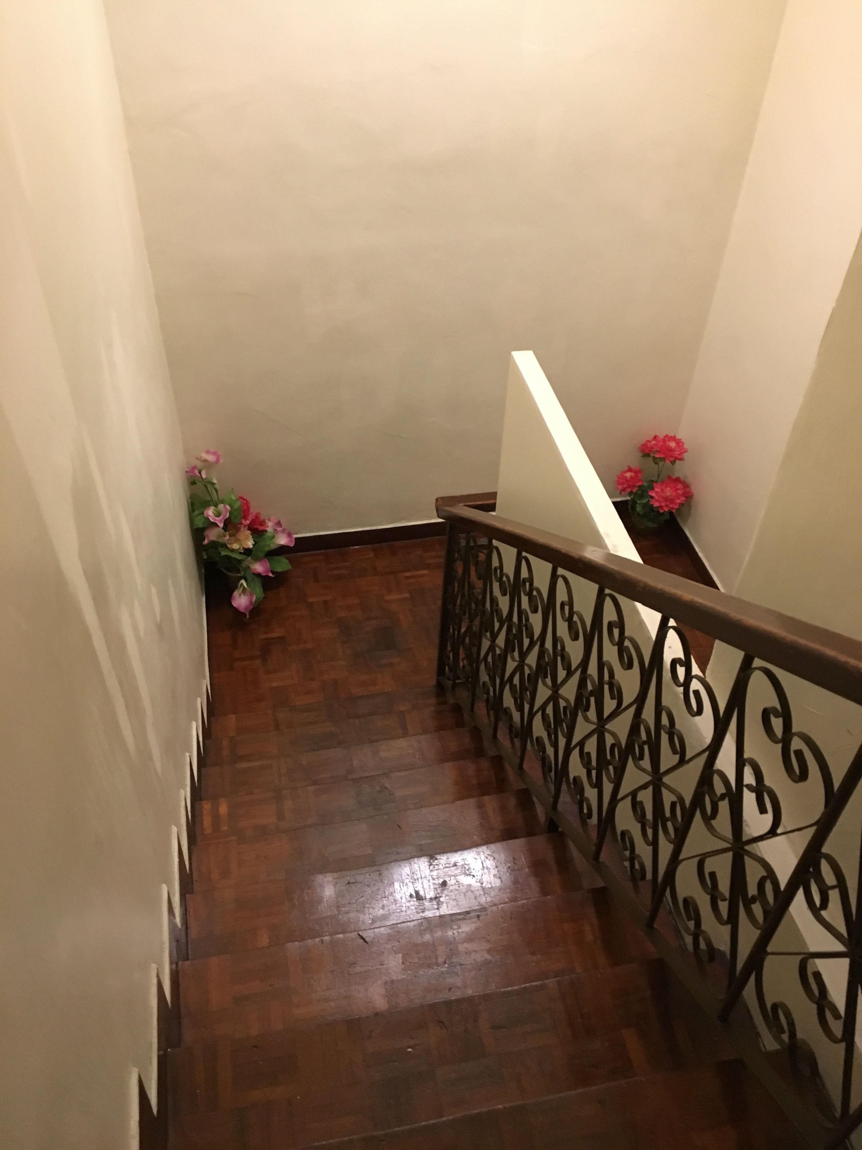 Un escalier en bois avec une rampe en métal, menant à un palier agrémenté d’une petite composition florale.