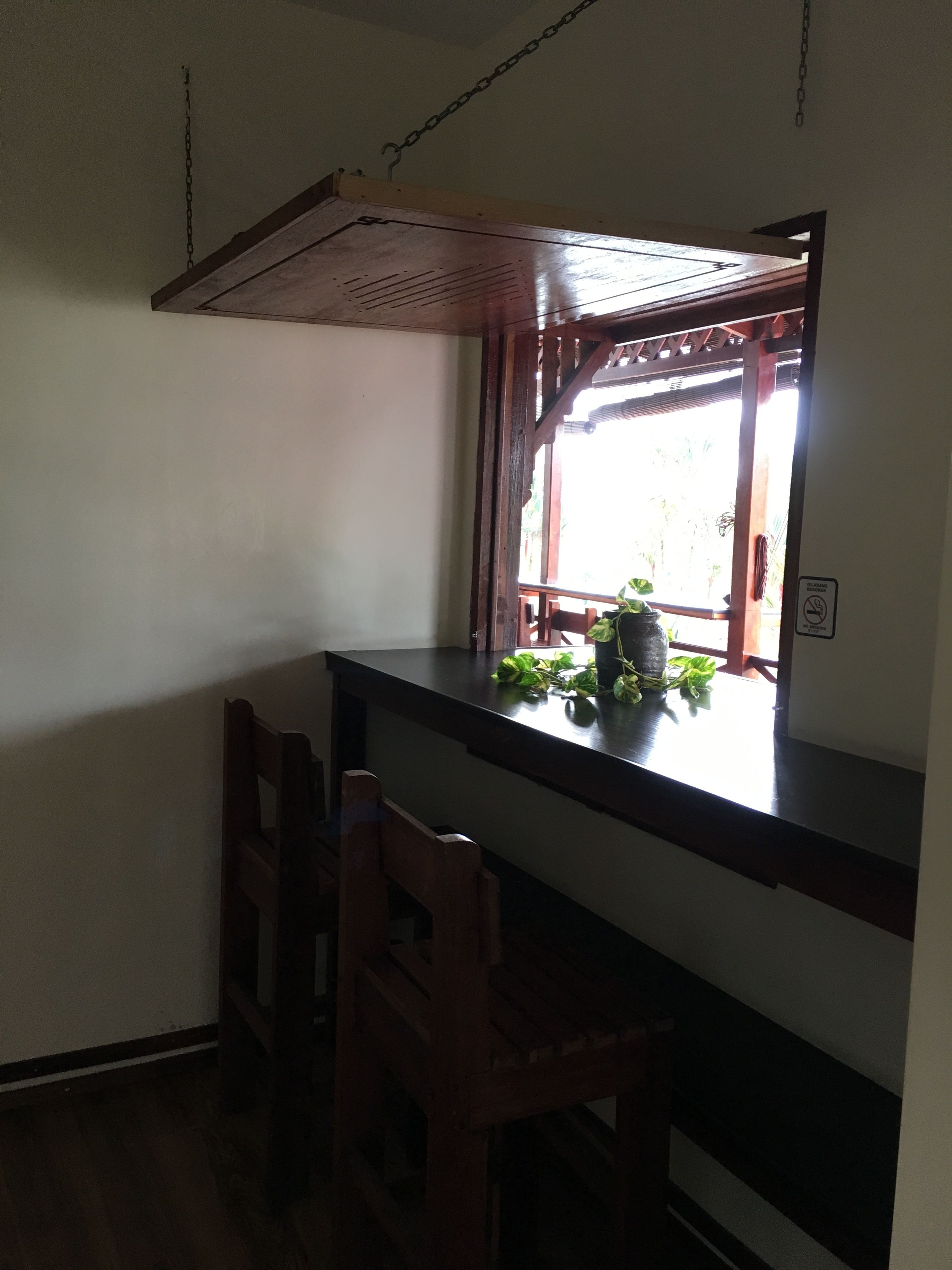 A kitchen with a wooden counter, a window with a view of greenery, and a hanging pot rack.