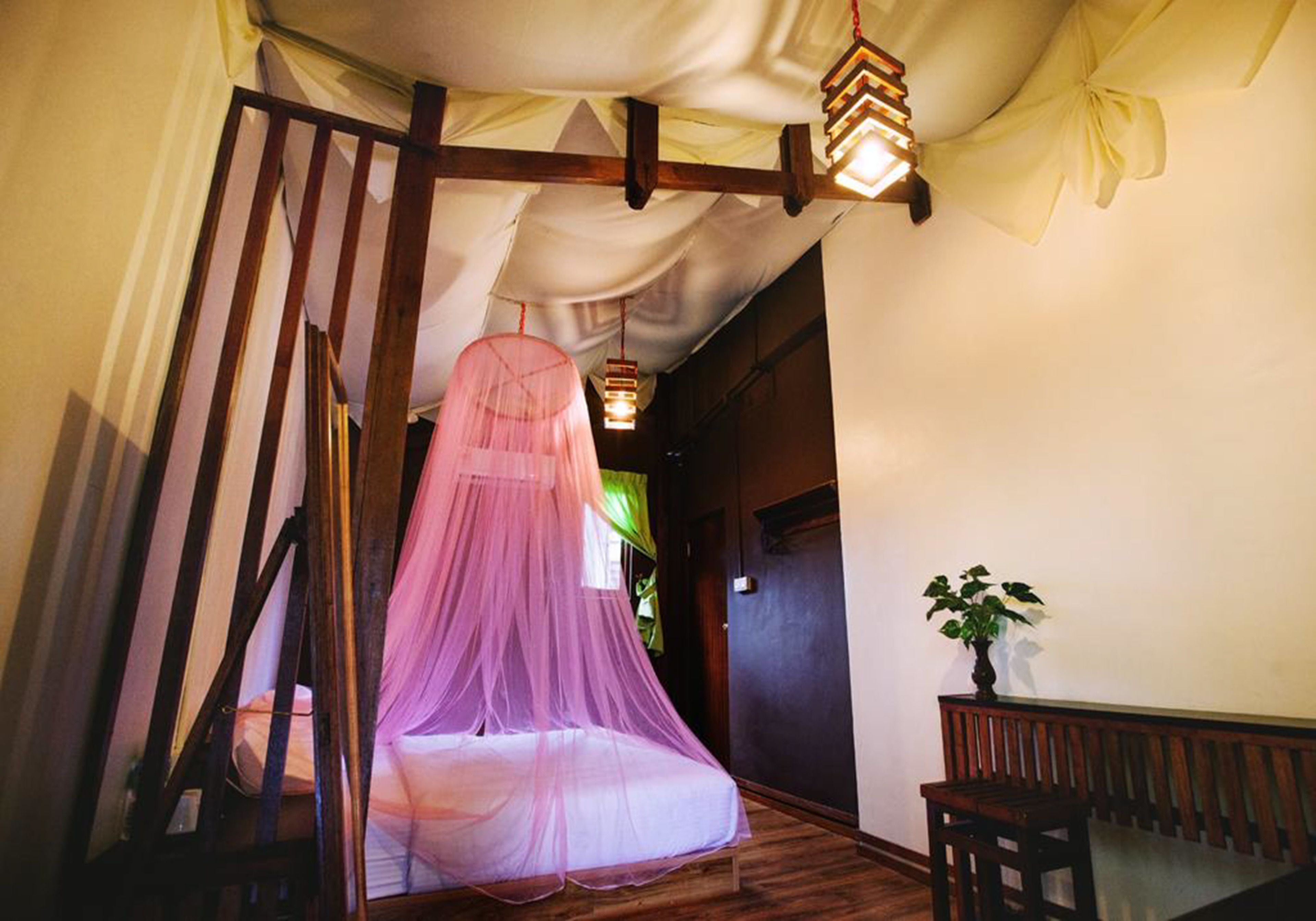 A room with a bed under a pink canopy, wooden beams, and a hanging light fixture.