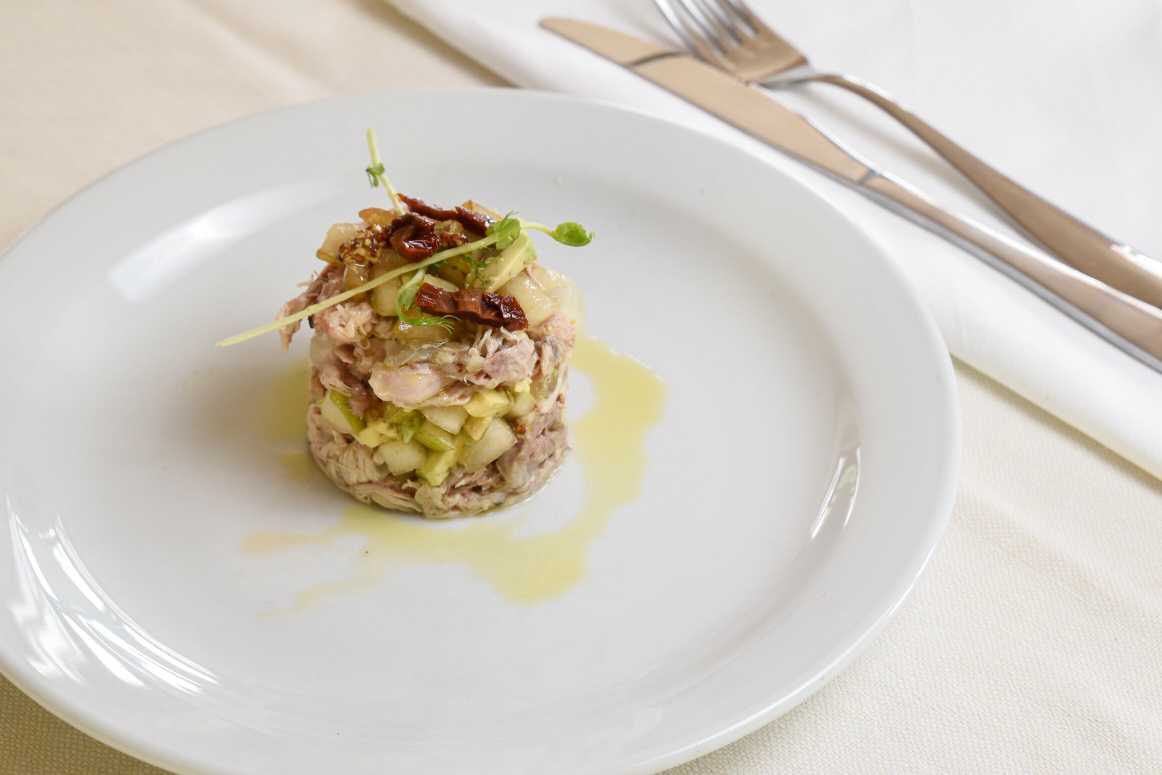 Un plato blanco con un guiso en capas, posiblemente un tartare, adornado con hierbas y un chorrito de salsa.