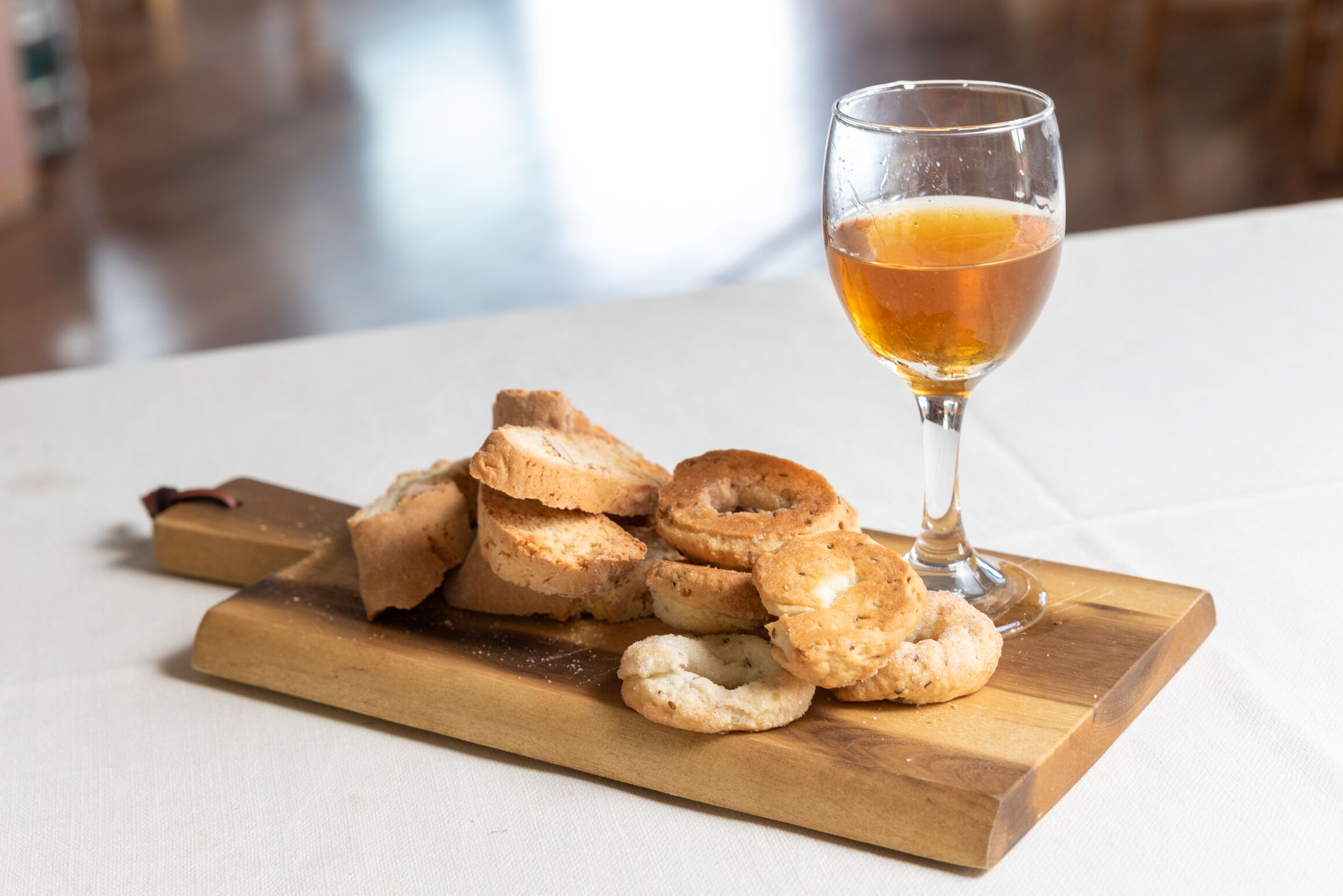 A wooden board with pastries and a glass of amber liquid on a table.