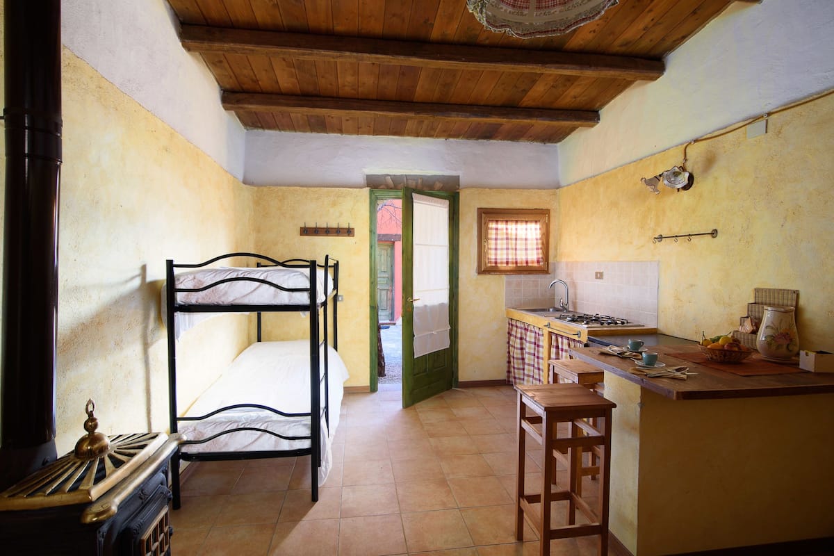 Una habitación compacta con literas, un kitchenette pequeño con lo esencial y techo de madera.