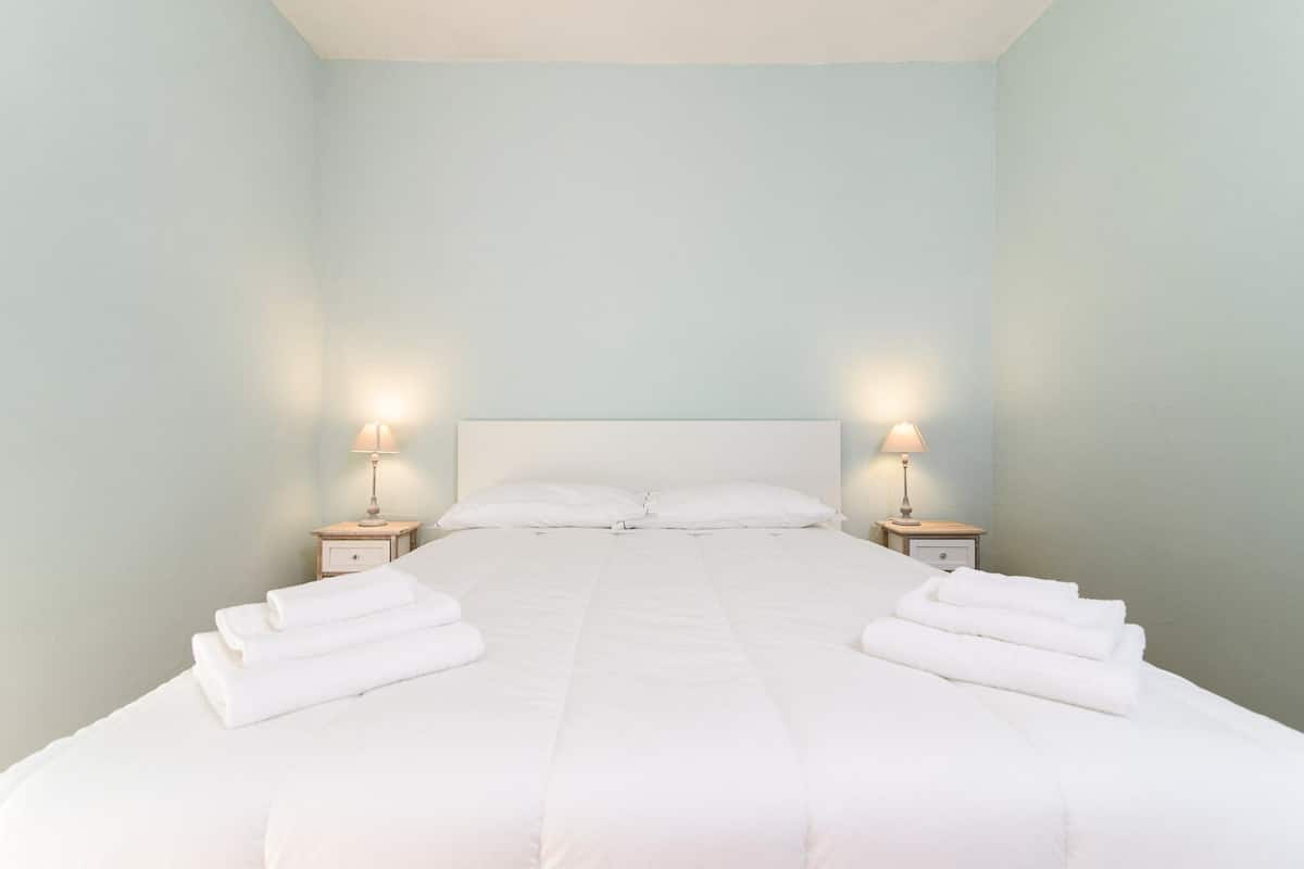 Una cama bien hecha con sábanas blancas y dos lámparas de noche.