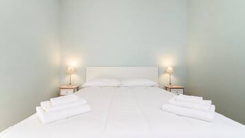 Un lit bien fait, avec du linge de lit blanc et deux lampes de chevet.