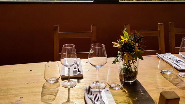 Una mesa de comedor al aire libre con copas de vino, cubiertos y un jarrón de flores.