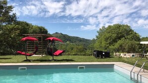 Una piscina con agua cristalina azul, rodeada por un césped con sombrillas rojas y una estructura de madera.