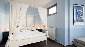 A bedroom with a four-poster bed, a nightstand, a bedside table, a framed picture on the wall, and a window.