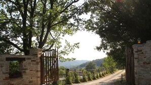 Una rústica puerta de piedra que da a un sendero rodeado de exuberante vegetación y un telón de fondo montañoso.