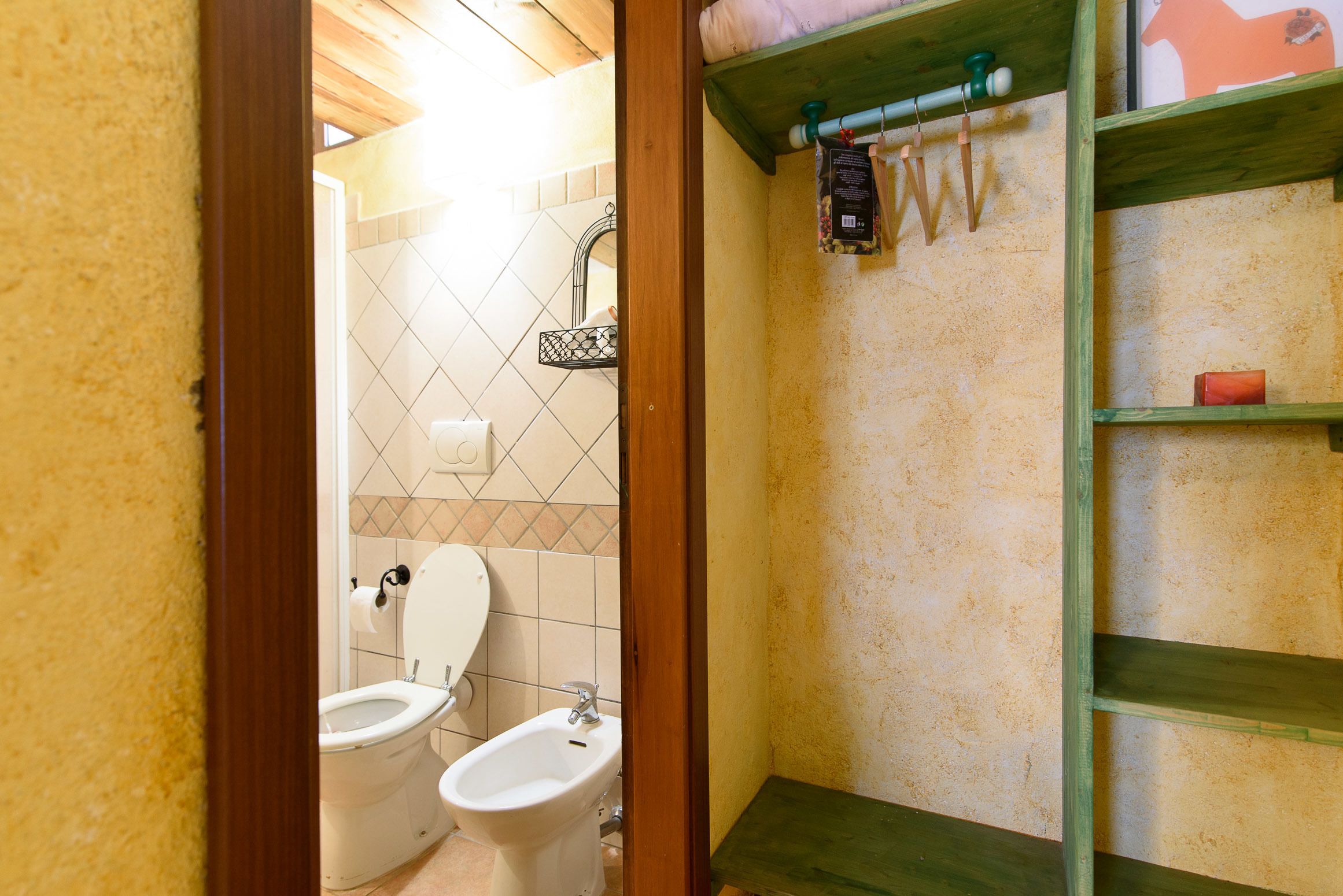 A bathroom with a toilet, bidet, and a shelf with toiletries.