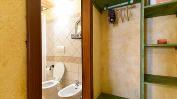 A bathroom with a toilet, bidet, and a shelf with toiletries.