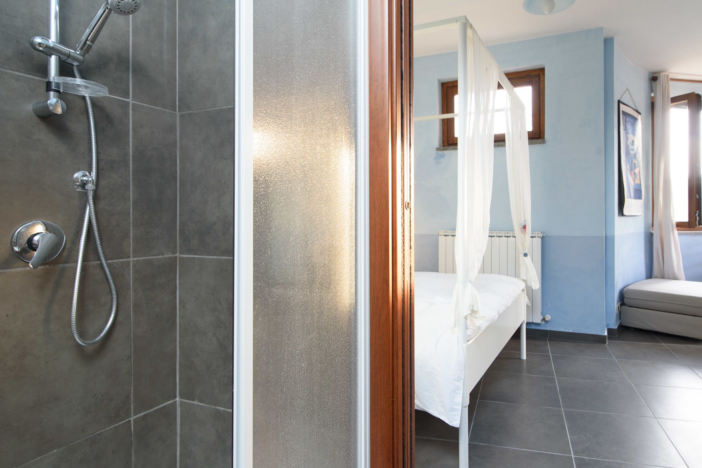 A bathroom with a shower, a bed, and a window.