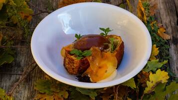 A white bowl with a dark sauce and a piece of bread on a wooden surface surrounded by autumn leaves.