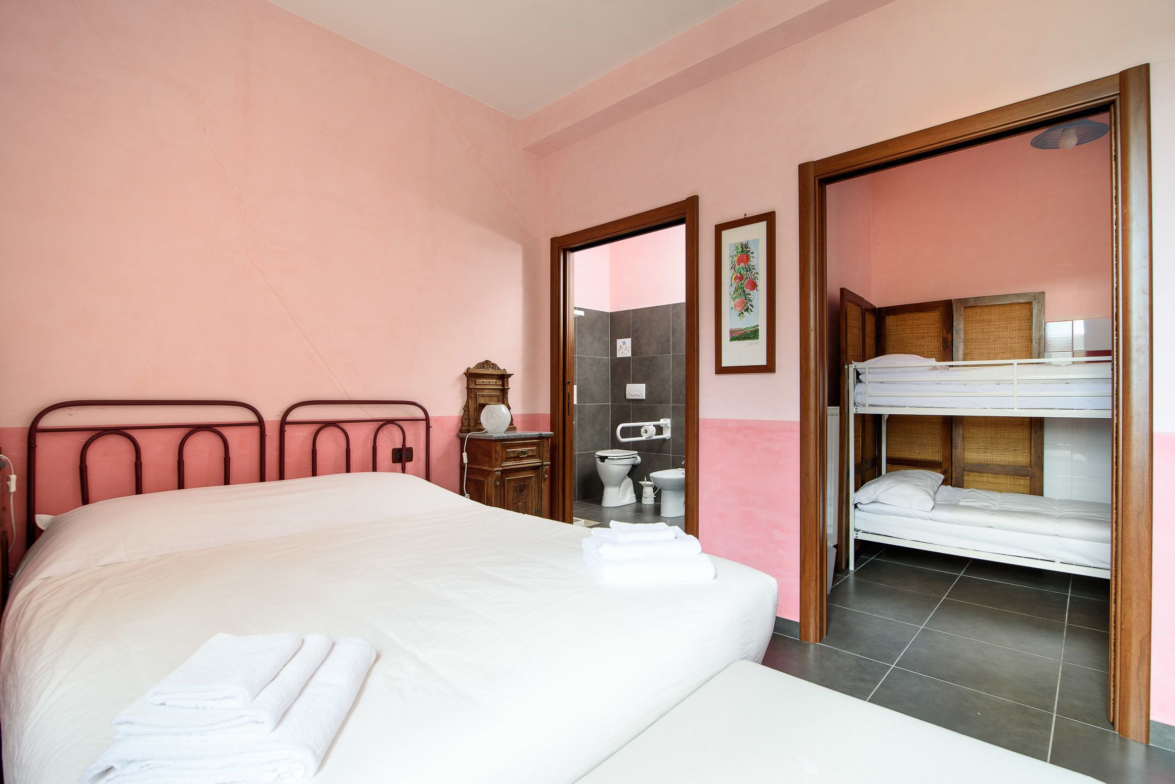 A hotel room with a large bed, a smaller bed, a wooden dresser, a mirror, and a bathroom visible through an open door.