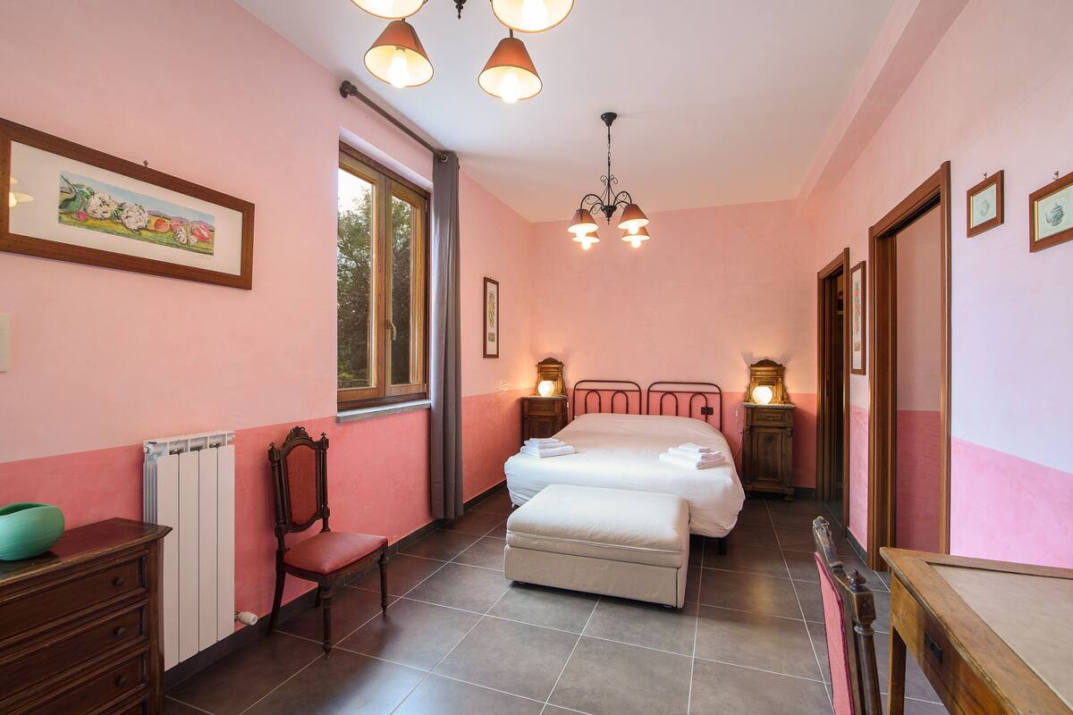 Un dormitorio con cama, una silla, tocador, radiador y ventana.