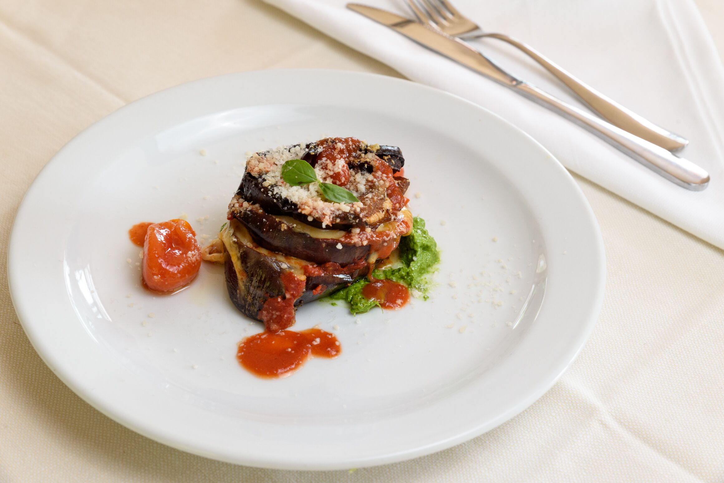 Un plato con berenjena rellena, adornado con hierbas y salsa, sobre un plato blanco.